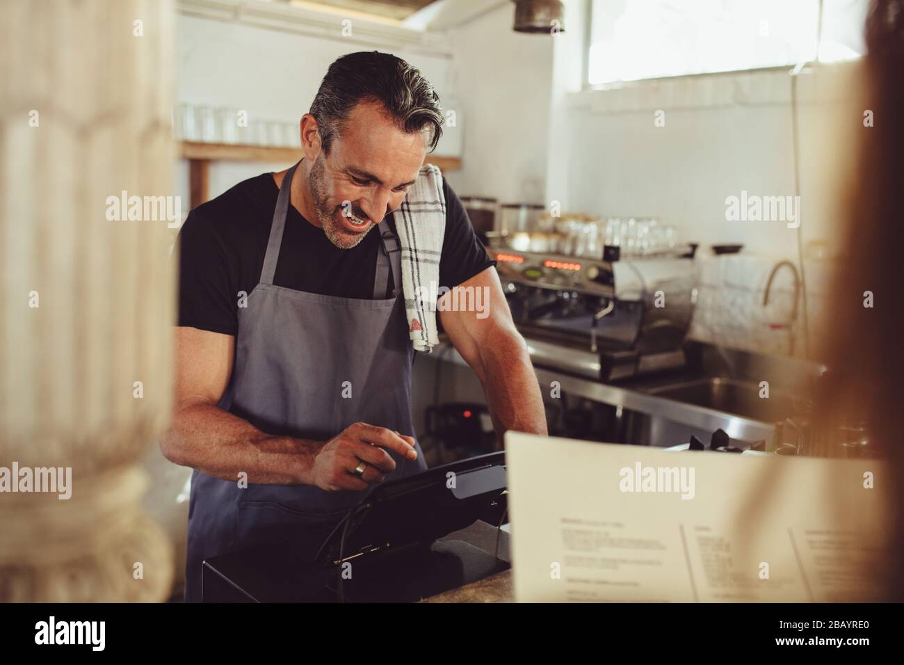 Cafe owner taking order from customer at coffee shop counter. Barista entering customer order in