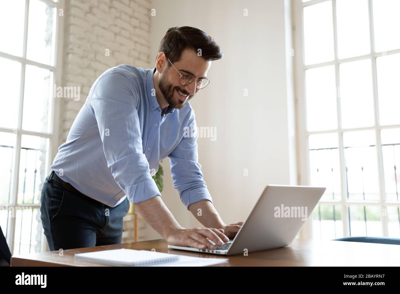 Businessman leaning over table in boardroom responds on business email Stock Photo