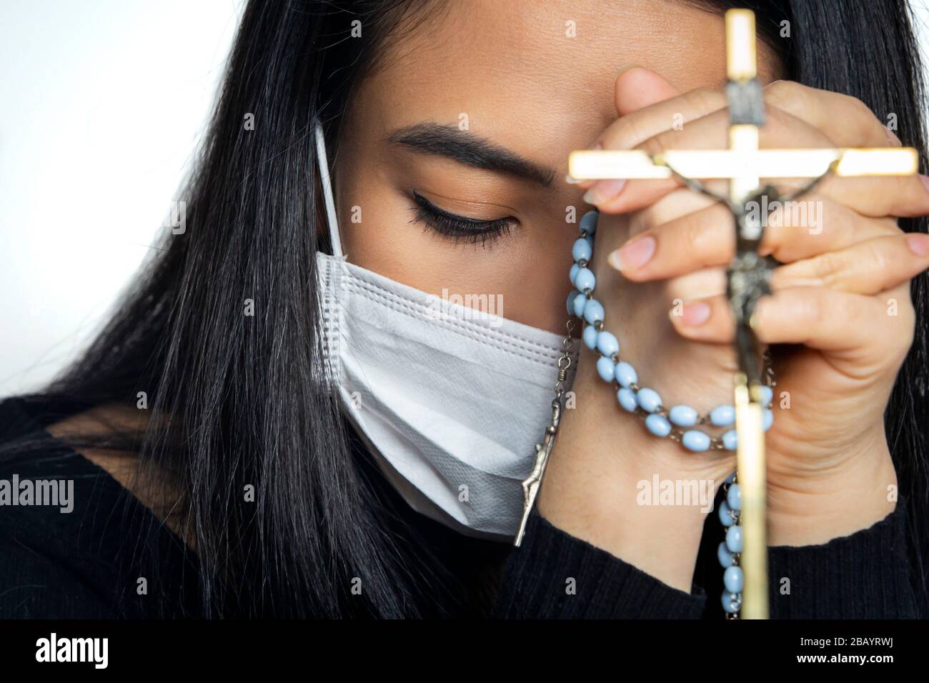 Woman wearing surgical mask praying with rosary. Christian religion hope concept. Stock Photo
