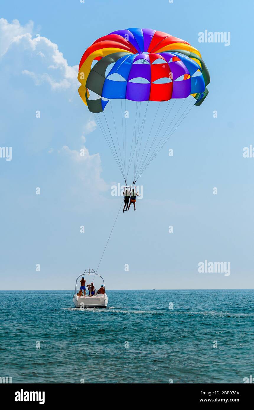 Holiday makers para sailing from power boat with colourful parachute
