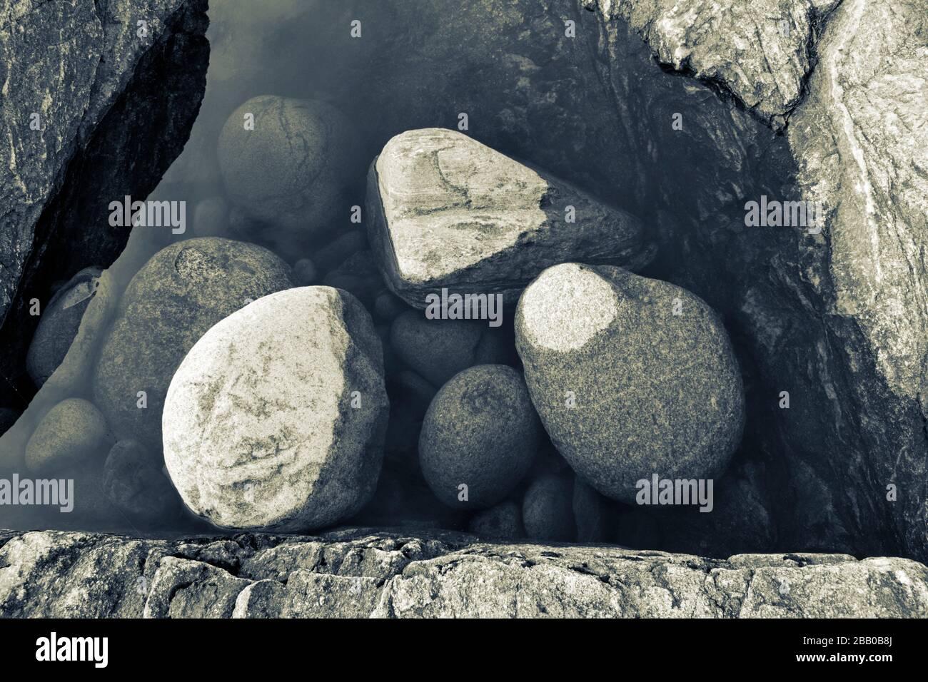 Stones are lying in a puddle on a rocky beach - duotone blue and yellow. Västernorrland, Sweden, Europe Stock Photo
