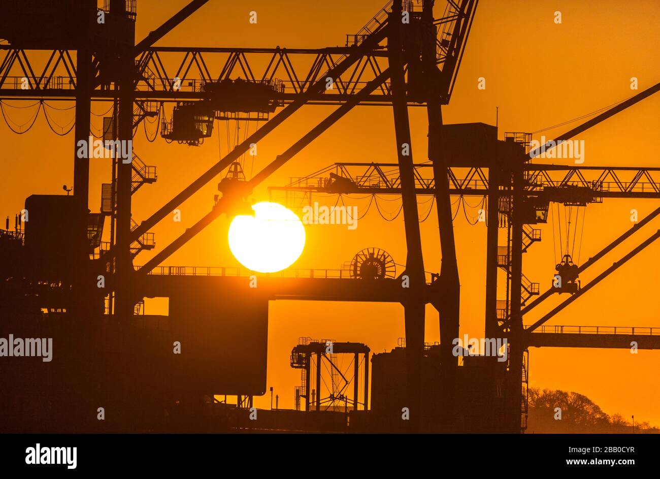 Tivoli, Cork, Ireland. 30th March, 2020. In critical times during the Covid-19 emergency the Irish economy is dependent on imports which are a lifeline to the country. Keeping this vital supply line open is the Port of Cork where the majority of the countries imports arrive.   Picture shows Gantry Cranes silhouetted by the rising sun at Tivoli Docks in Cork City, Ireland.    - Credit; David Creedon / Alamy Live News Stock Photo