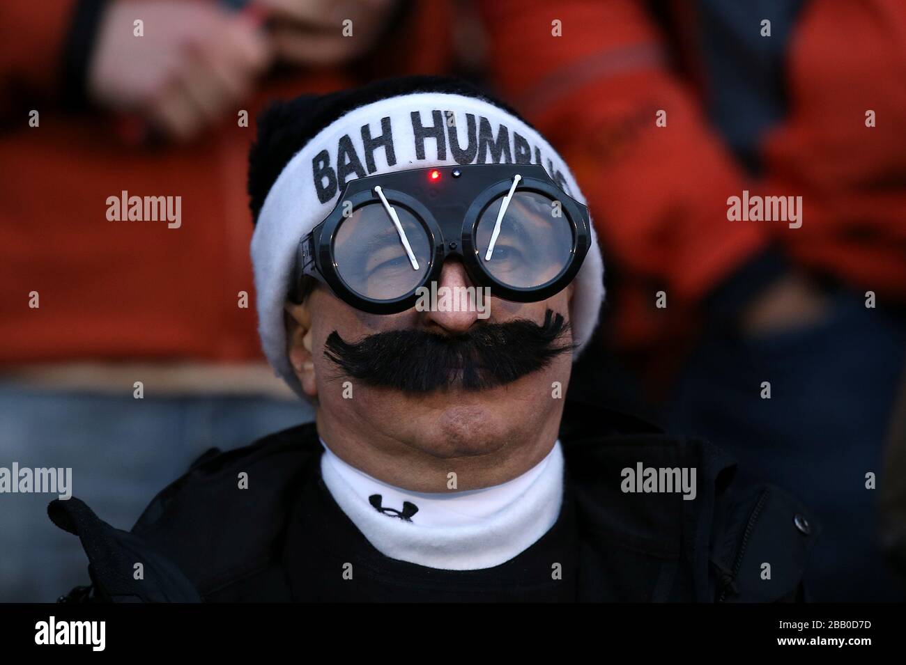 A Fulham fan wears a Christmas hat that says 'Bah Humbug' as well as aviator goggles and a moustache Stock Photo