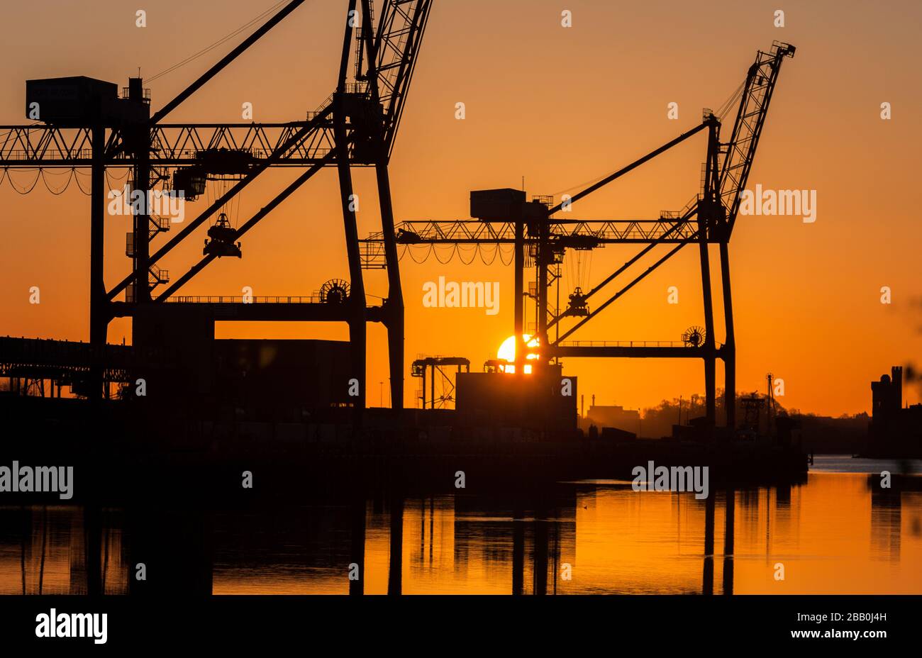 Tivoli, Cork, Ireland. 30th March, 2020. In critical times during the Covid-19 emergency the Irish economy is dependent on imports which are a lifeline to the country. Keeping this vital supply line open is the Port of Cork where the majority of the countries imports arrive.   Picture shows Gantry Cranes silhouetted by the rising sun at Tivoli Docks in Cork City, Ireland.    - Credit; David Creedon / Alamy Live News Stock Photo