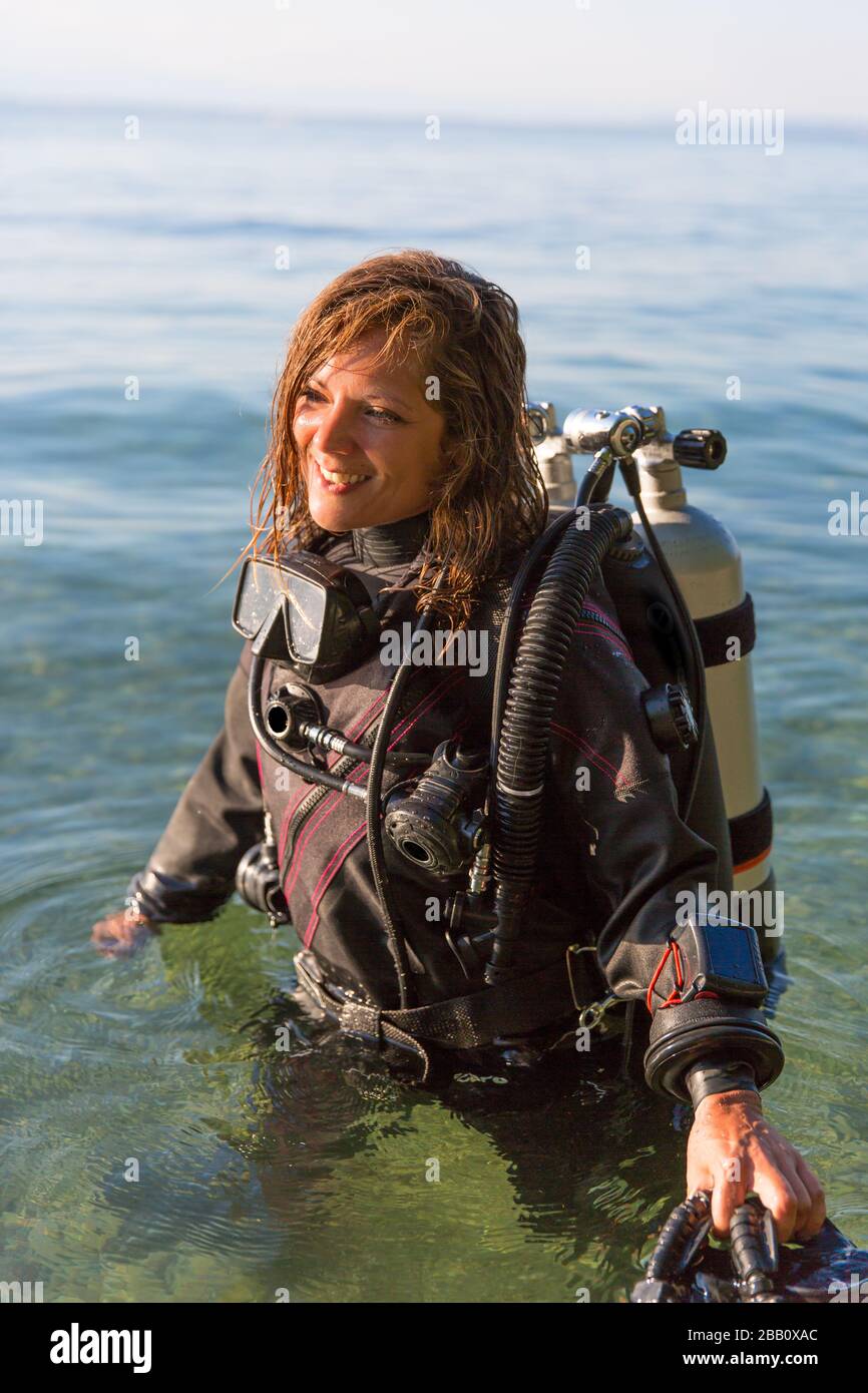 Female Scuba Diving Instructor Standing in Water Wearing a Dry Suit, a Twin Tank and Holding Fins Stock Photo