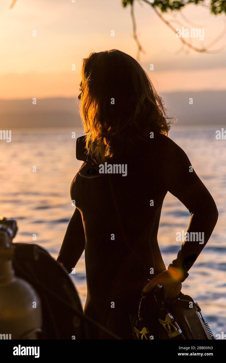 Female Scuba Diving Instructor Wearing a Wet Suit Standing Next to a Twin Tank at Sunset Stock Photo