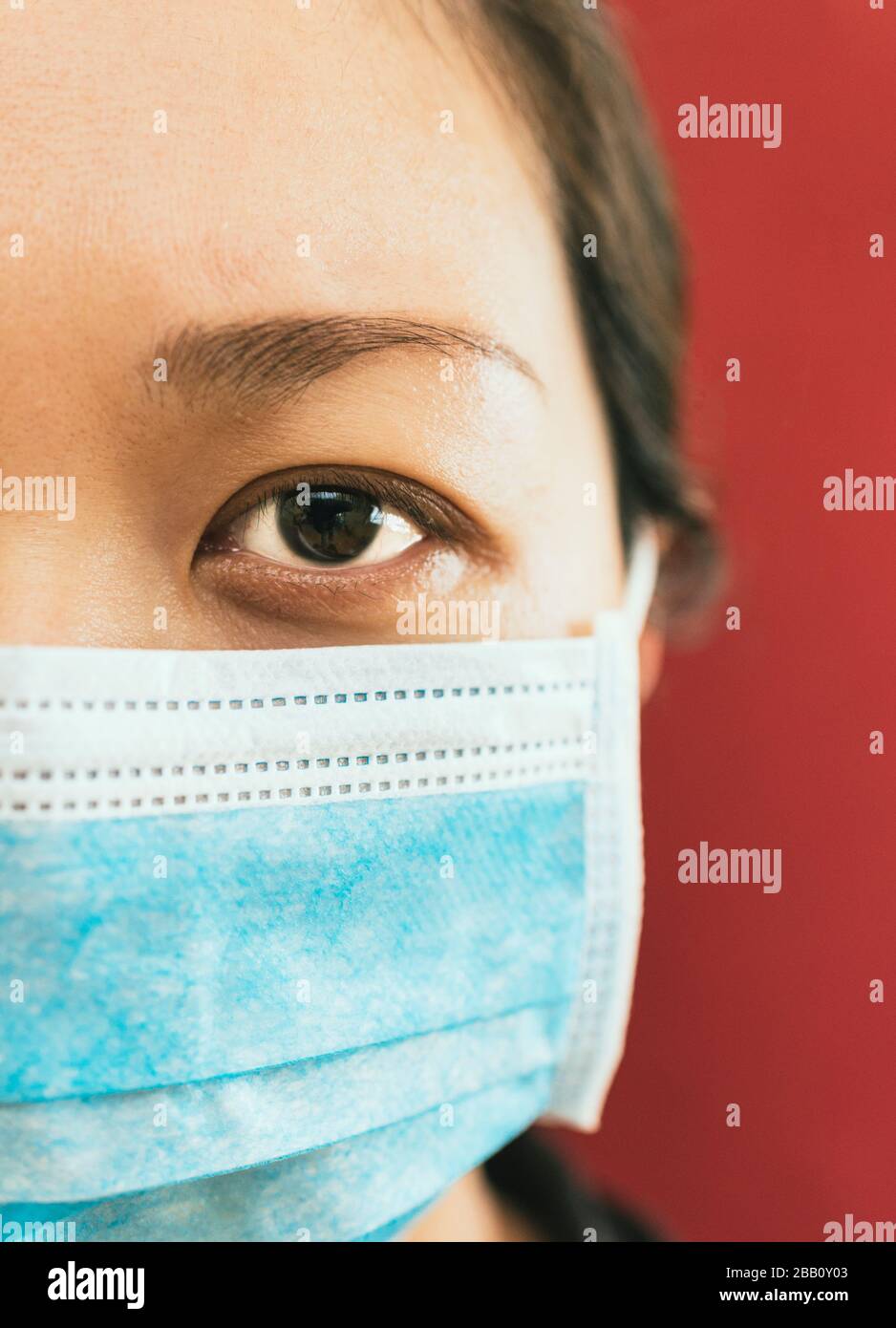 Coronavirus theme. Asian woman  wearing a mask to protect herself from getting infected on a red background. Stock Photo
