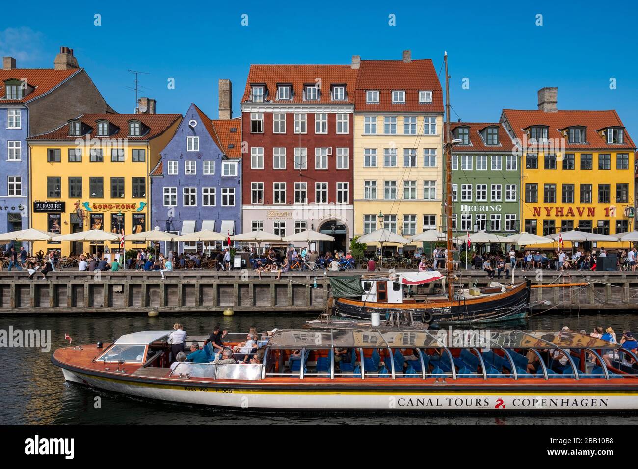 A canal tour boat navigates through a canal in Copenhagen, showing historic buildings and bridges along the water.