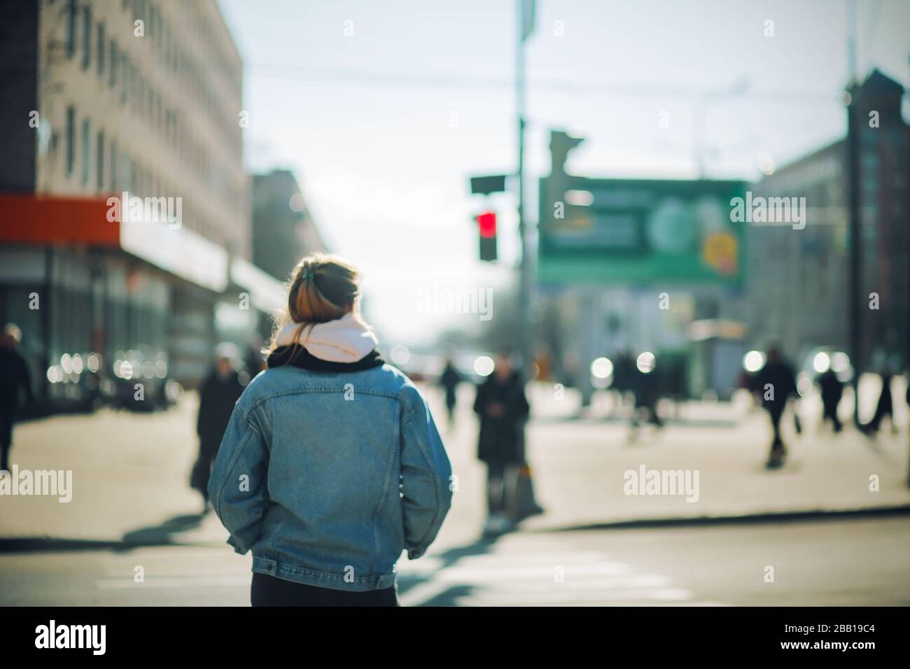 A blurry image of a girl in fashionable clothes standing in front of a pedestrian crossing and waiting for a green light on a Sunny spring day. Stock Photo