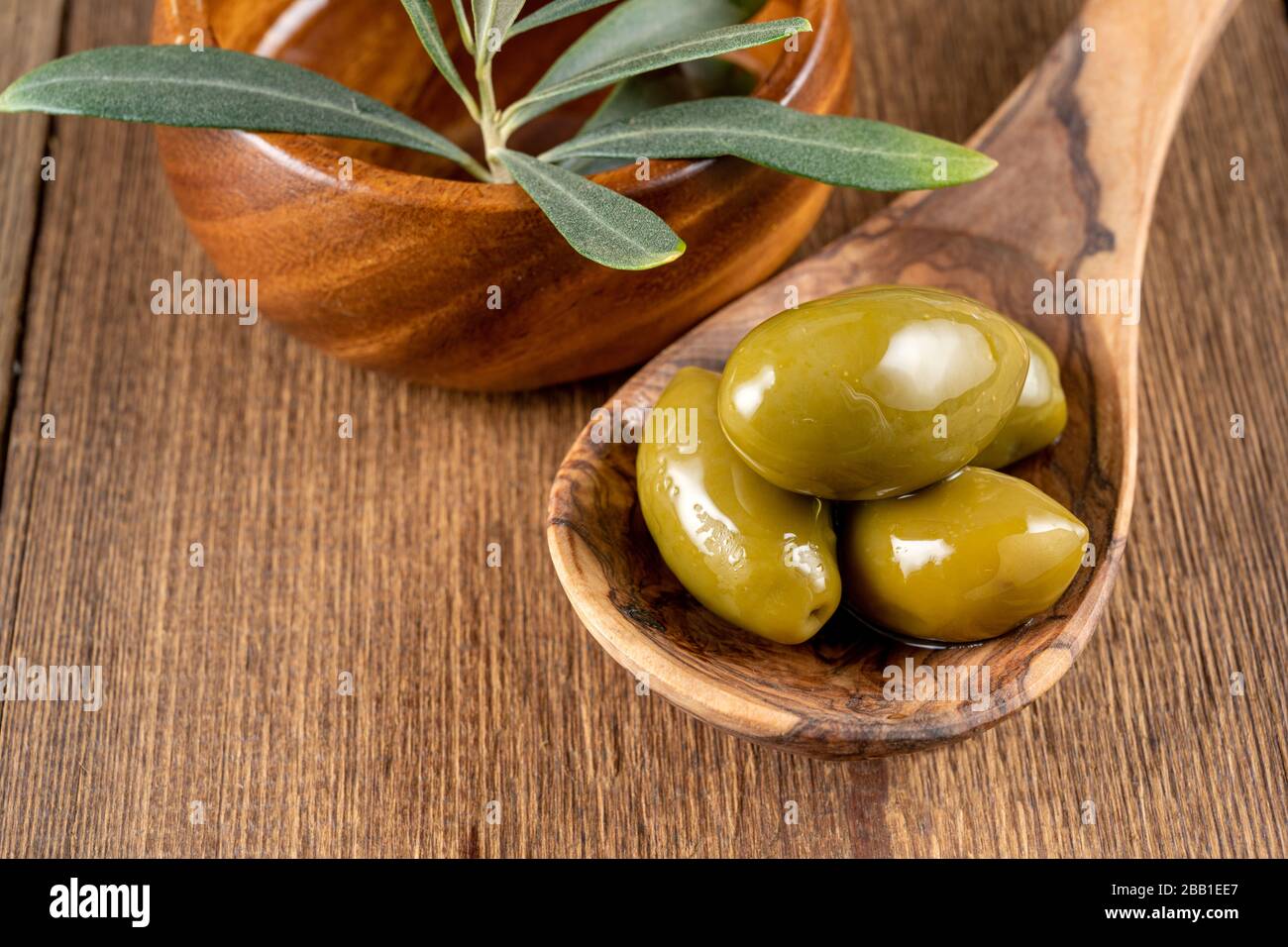 Green olives on a wooden cooking spoon and an olive branch in a wooden ...