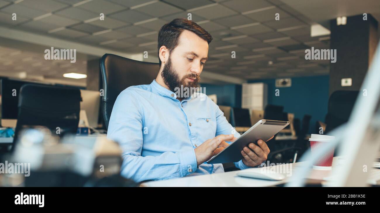 Caucasian businessman with beard browsing on his tablet while working in the office Stock Photo