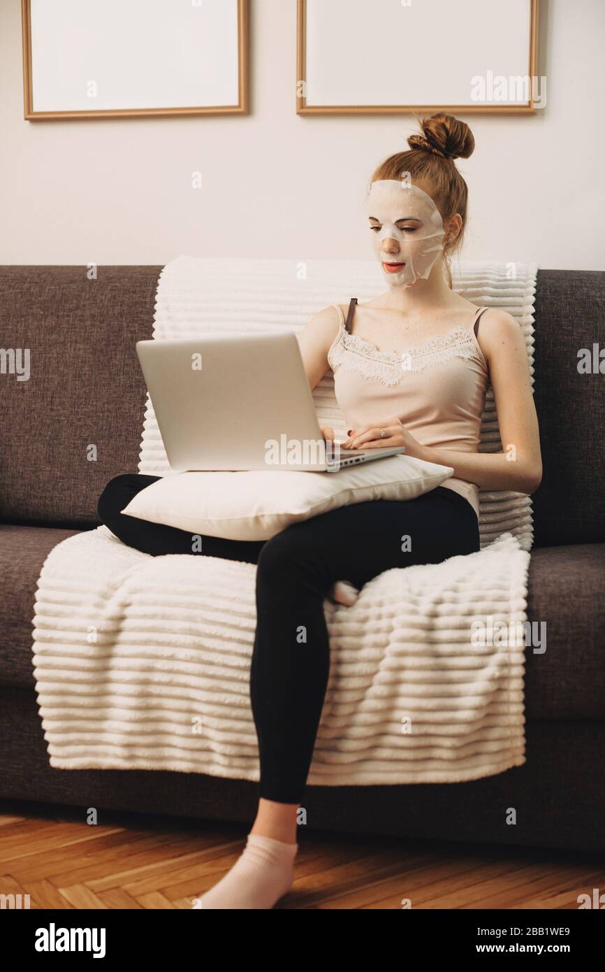 Caucasian woman wearing a special anti-wrinkle mask while sitting on the couch and using a computer Stock Photo