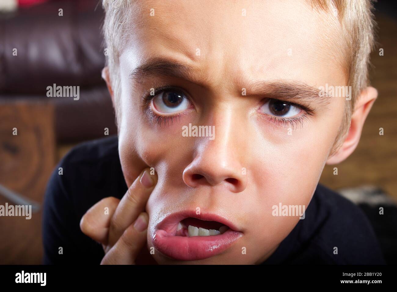 A headshot closeup photo of a beautiful young boy with a very funny facial expression and just being silly. He has hazel brown eyes and blonde hair. Stock Photo