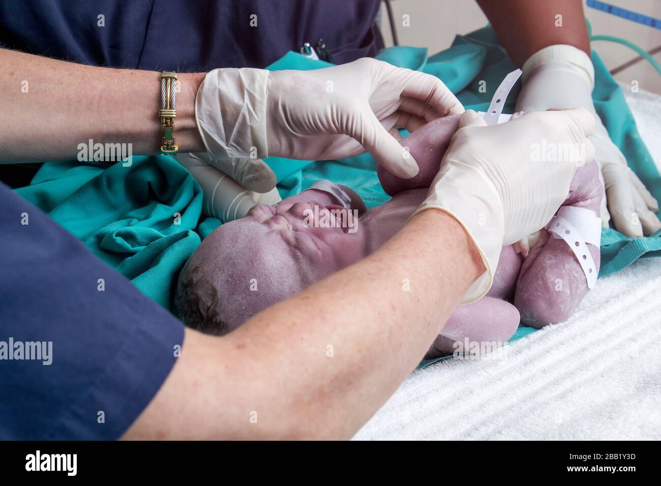 Doctors attending to newborn baby boy in hospital delivery room. He is laying on a bed while the doctors are attending to him and he is crying. Stock Photo