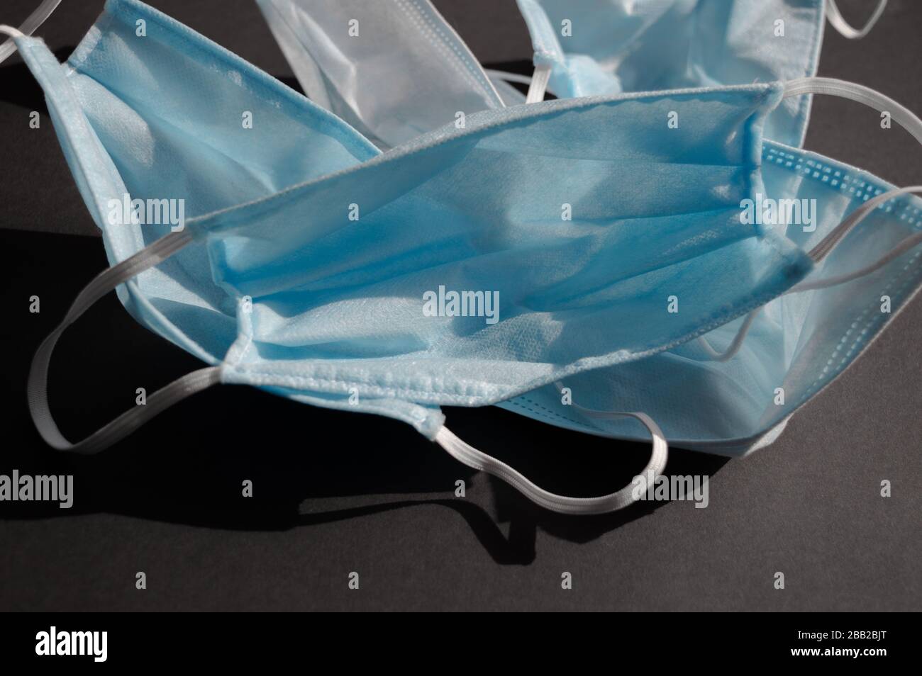 Five light blue used medical disposable face masks on the dark black background againts virus covid-2019. Heath care concept, quarantine, stop Stock Photo