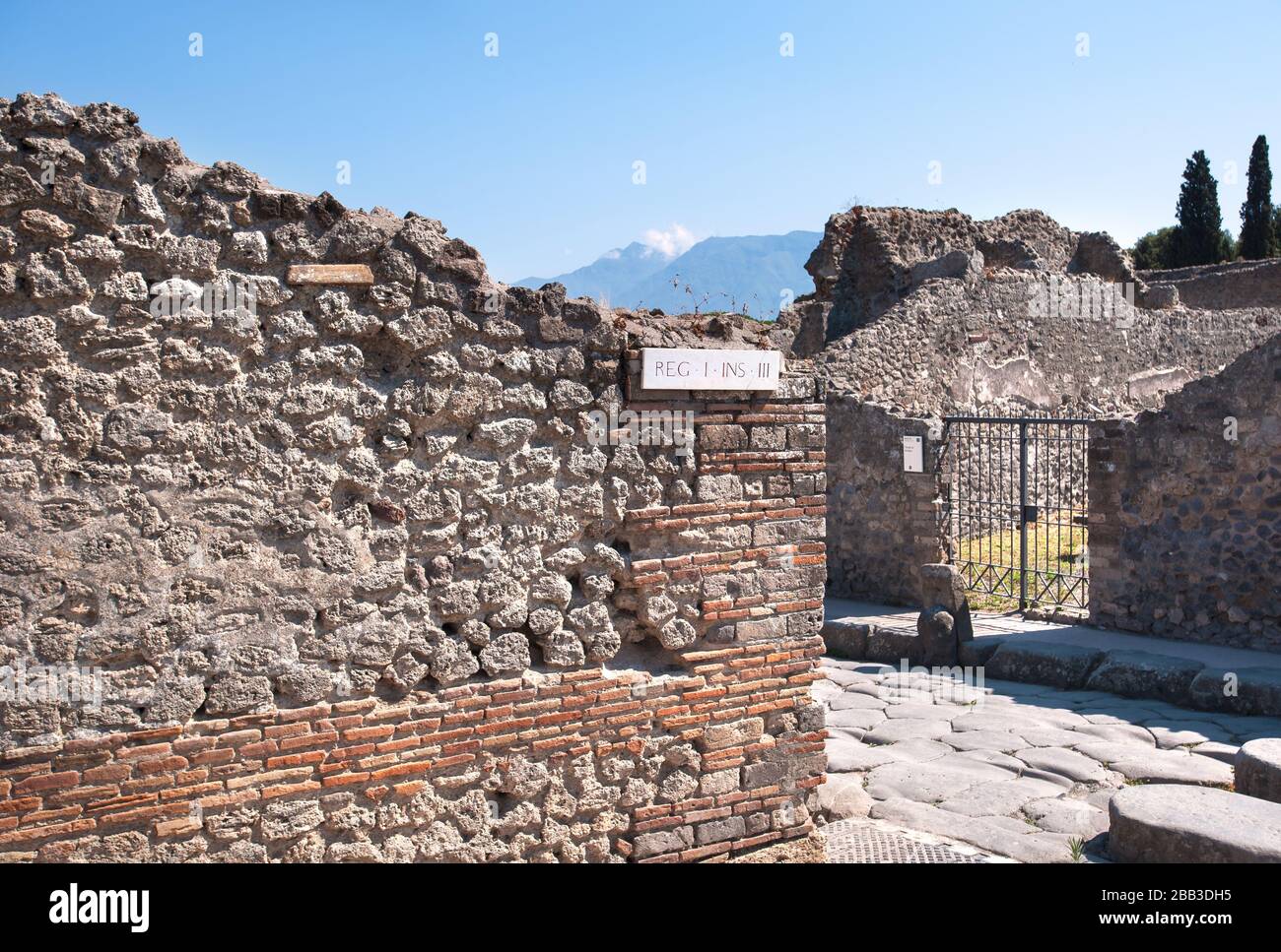 Ancient street and ruined houses in the ancient town of Pompeii, Italy. The peak of Mount Vesuvius can be seen in the background. Stock Photo