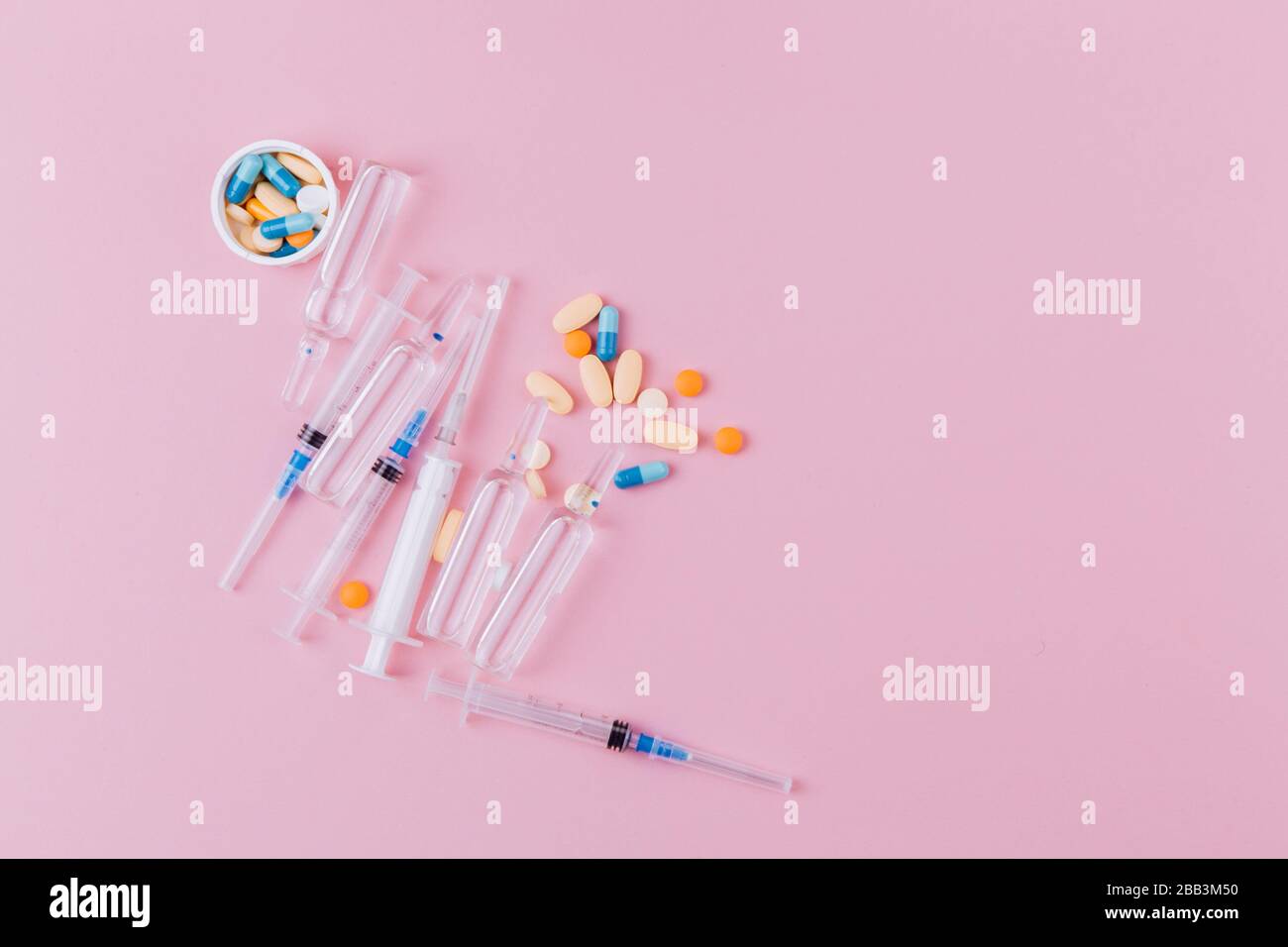Syringe and ampoules with medicine, a jar with a variety of pills on a pink background. poses a pandemic hazard. Stock Photo
