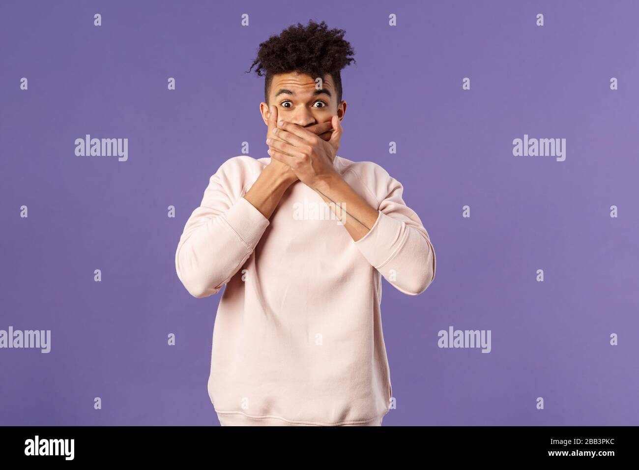Portrait of shocked impressed young hispanic man found out gossip, heard rumour, trying not laugh shut his mouth with hands and express amazement and Stock Photo