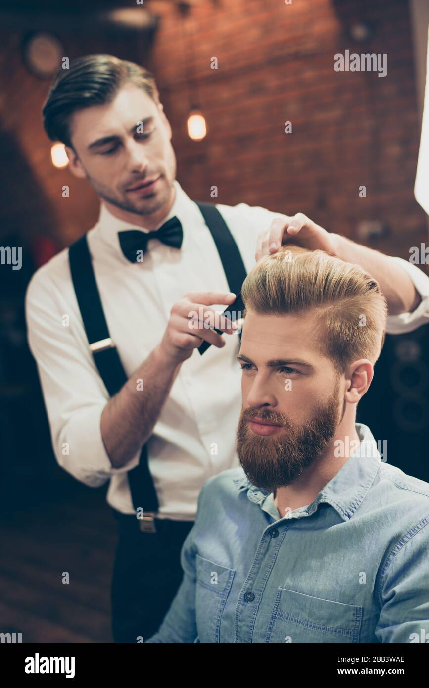 Barber shop classy dressed handsome stylist is doing a perfect hairstyle to  a bearded guy in caual jeans outfit. Both concentrated and serious Stock  Photo - Alamy