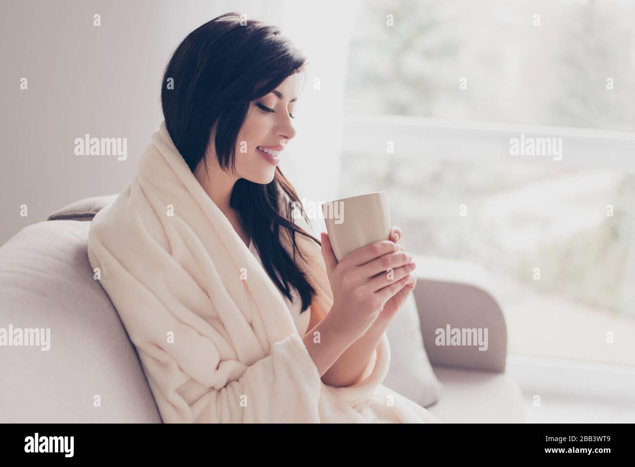 Morning is here! Close up profile portrait of cute brunette girl, smiling and holding a cup of coffee, covered with a plaid. Nice beginning of day Stock Photo