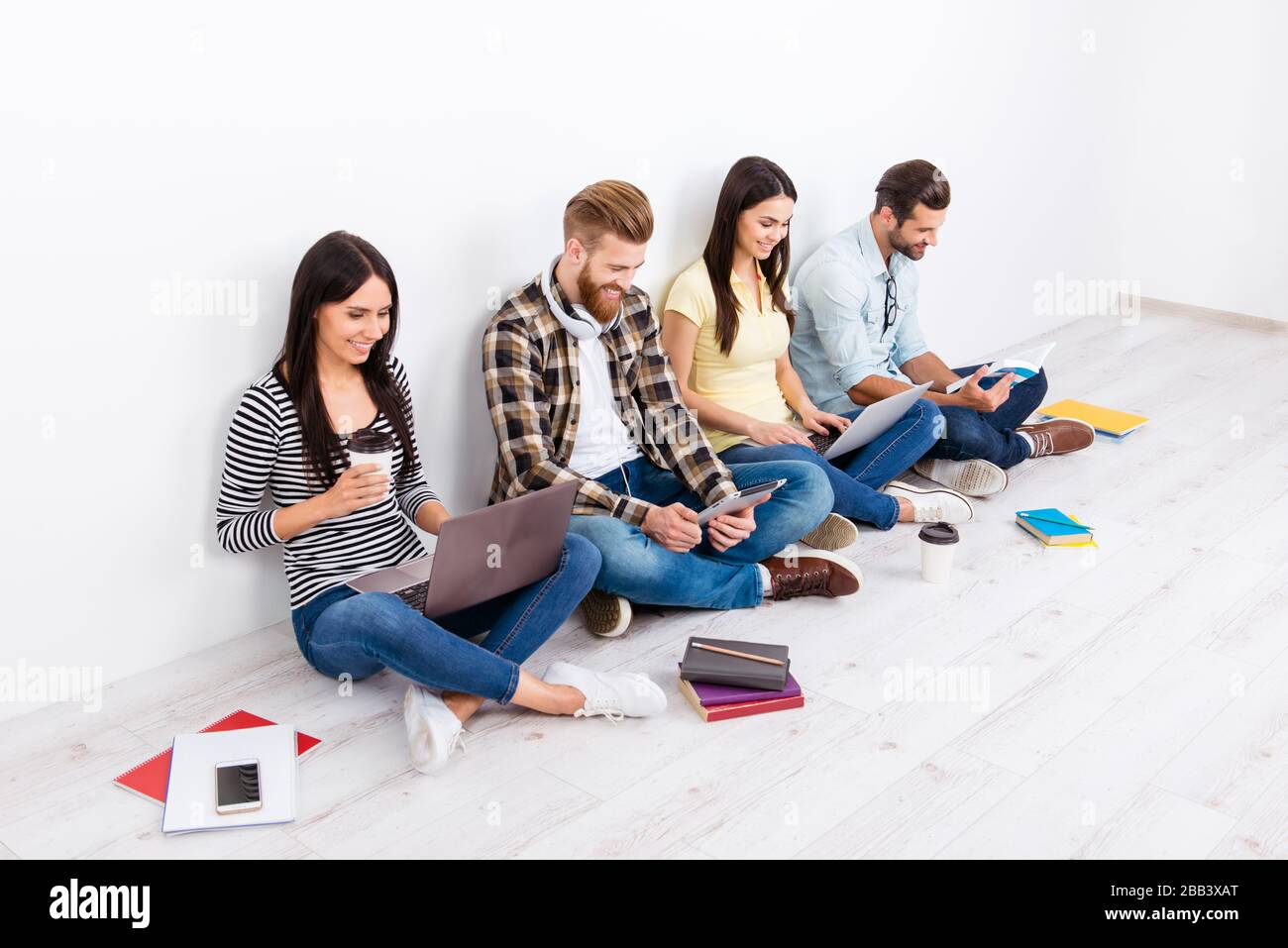 Company of happy students sitting on the floor with crossed legs studying and smiling. They are preparing to pass exams. It is more fun and easier to Stock Photo