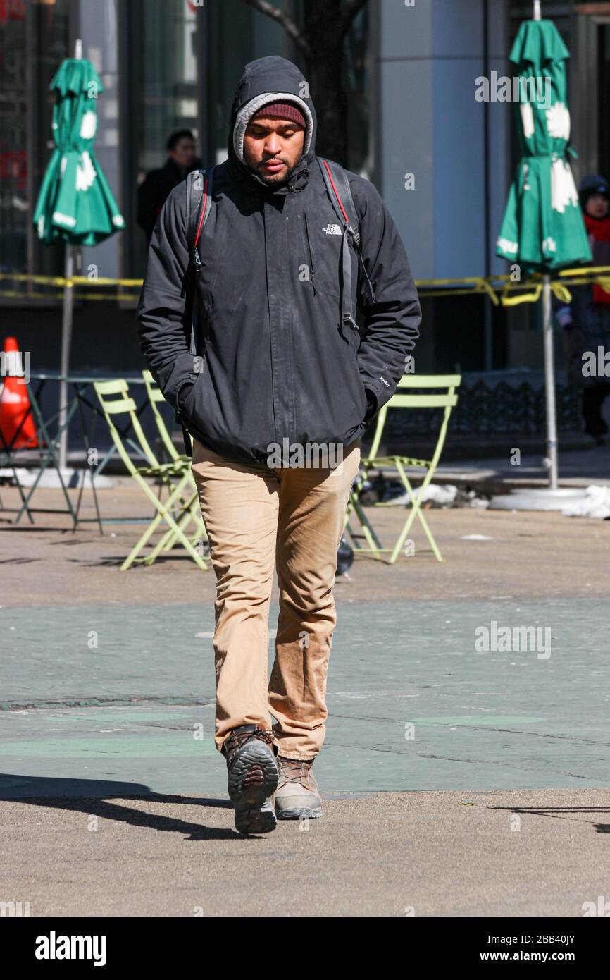 Young man walking with his hands in pocket and hood pulled up on a cold February day in Manhattan, New York City, United States of America Stock Photo