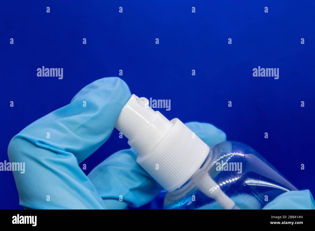 Spray disinfect liquid, hand in blue glove on blue background. Sanitize spray water drops. Prevent virus illness spread in air aerosol. Clean hands Stock Photo