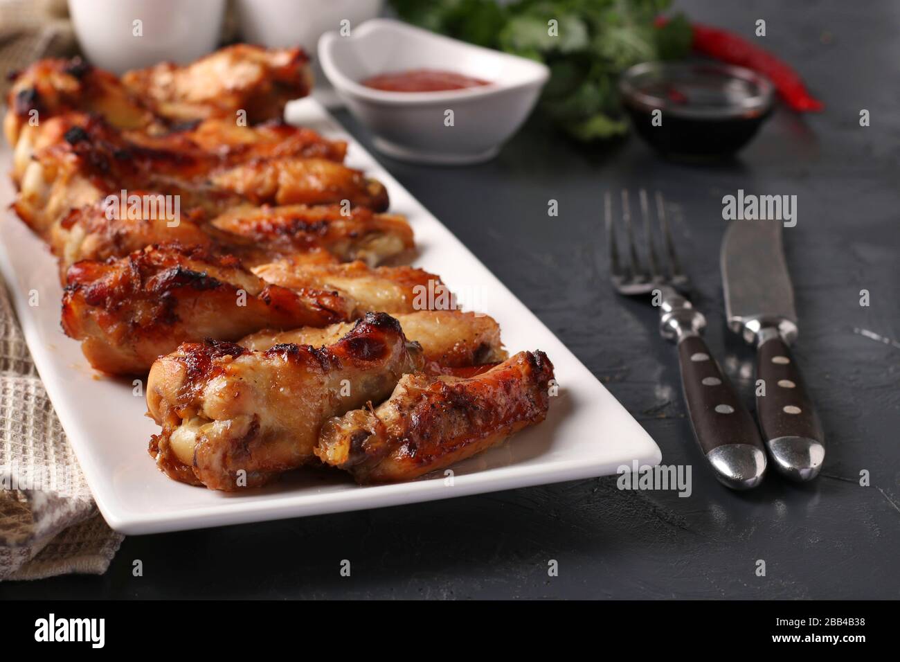 Grilled chicken wings on a white plate and tomato sauce on dark background Stock Photo