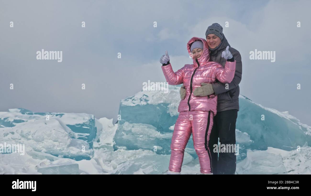 Couple has fun during winter walk against background of ice of frozen lake. Lovers lie on clear ice, have fun, kiss and hug. View from above. Stock Photo