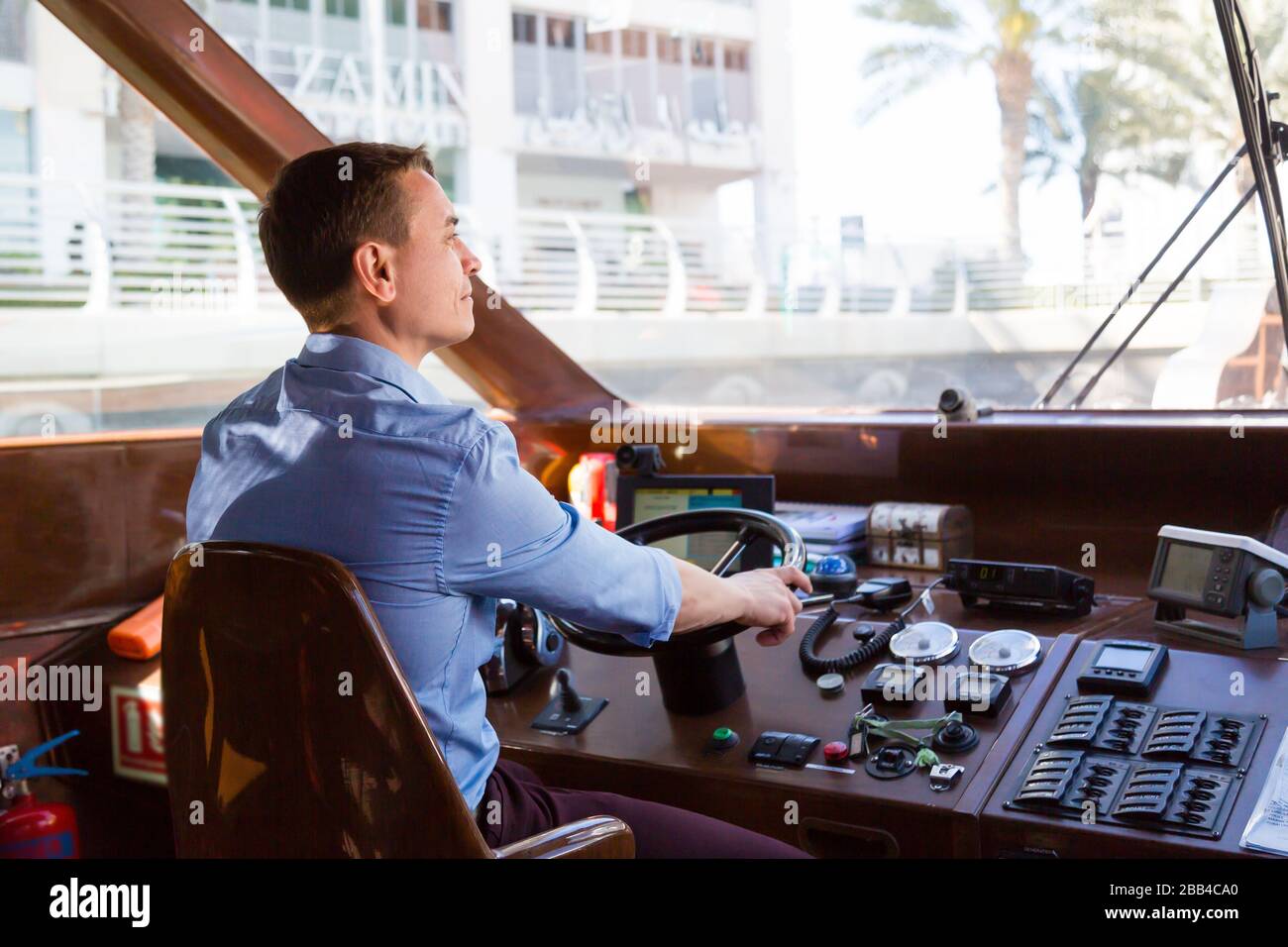 A male captain of a watercraft boat at the helm of a boat Stock Photo ...