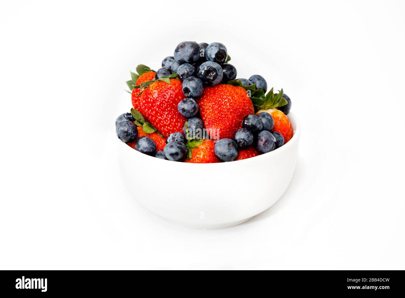 A white bowl full of delicious seasonal fruits, Blueberries, and Strawberries, mixed together. In a white background. For Healthy breakfast or snacks. Stock Photo