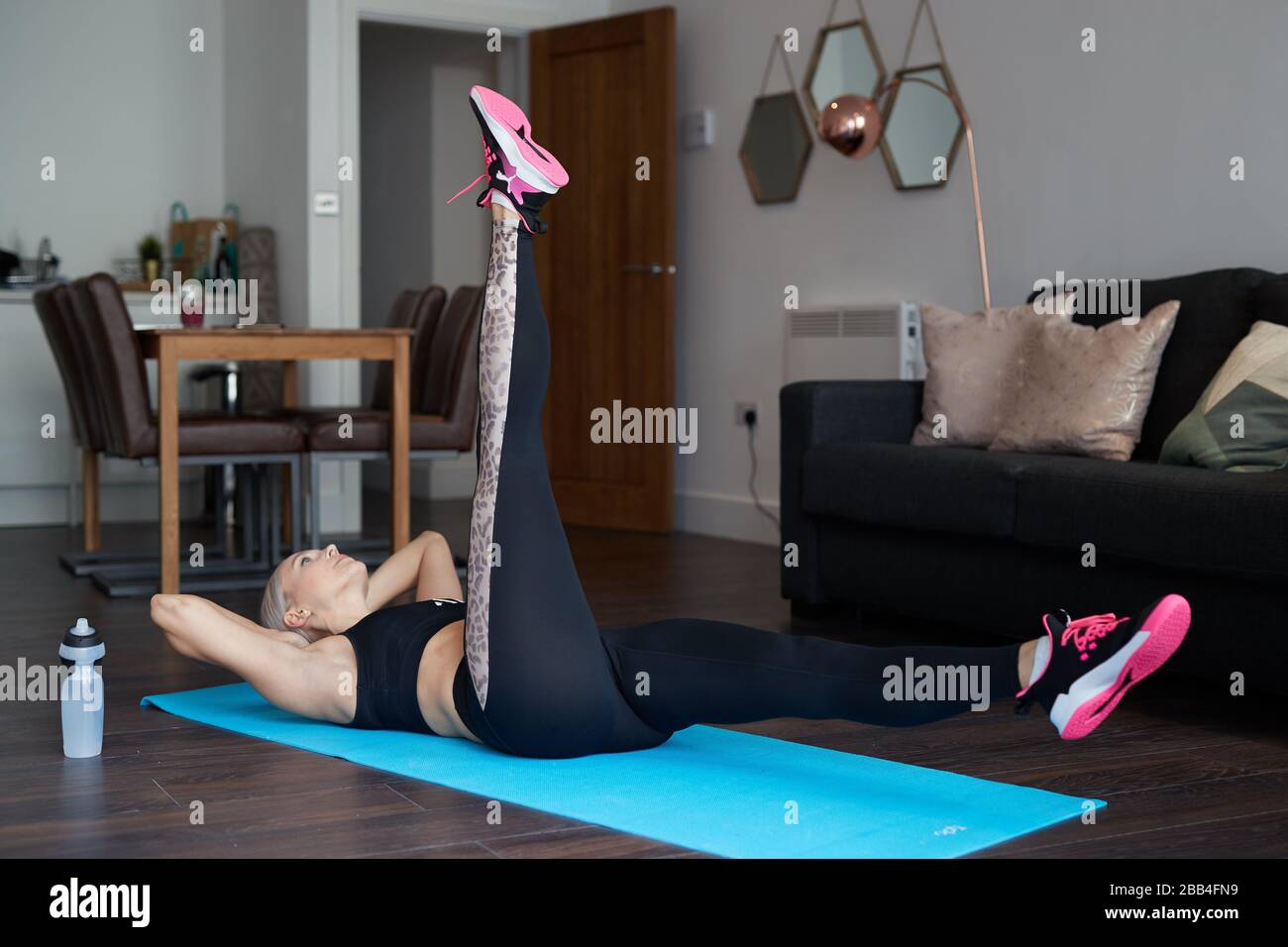 A Single Blonde female stretches as she exercises at home on a mat in the living room of her apartment Stock Photo