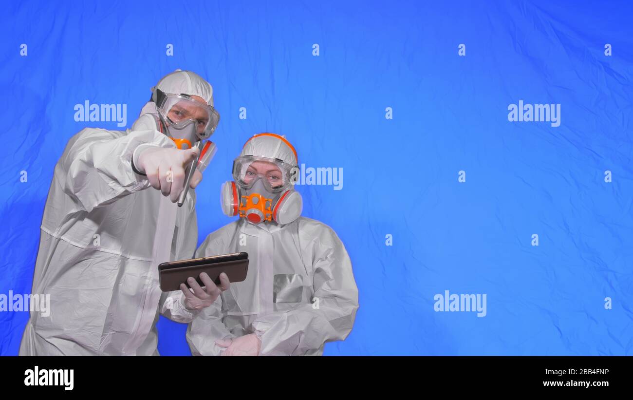 Scientist virologist in respirator makes write in an tablet computer with stylus. Man and woman wearing protective medical mask. Chroma key blue. Stock Photo