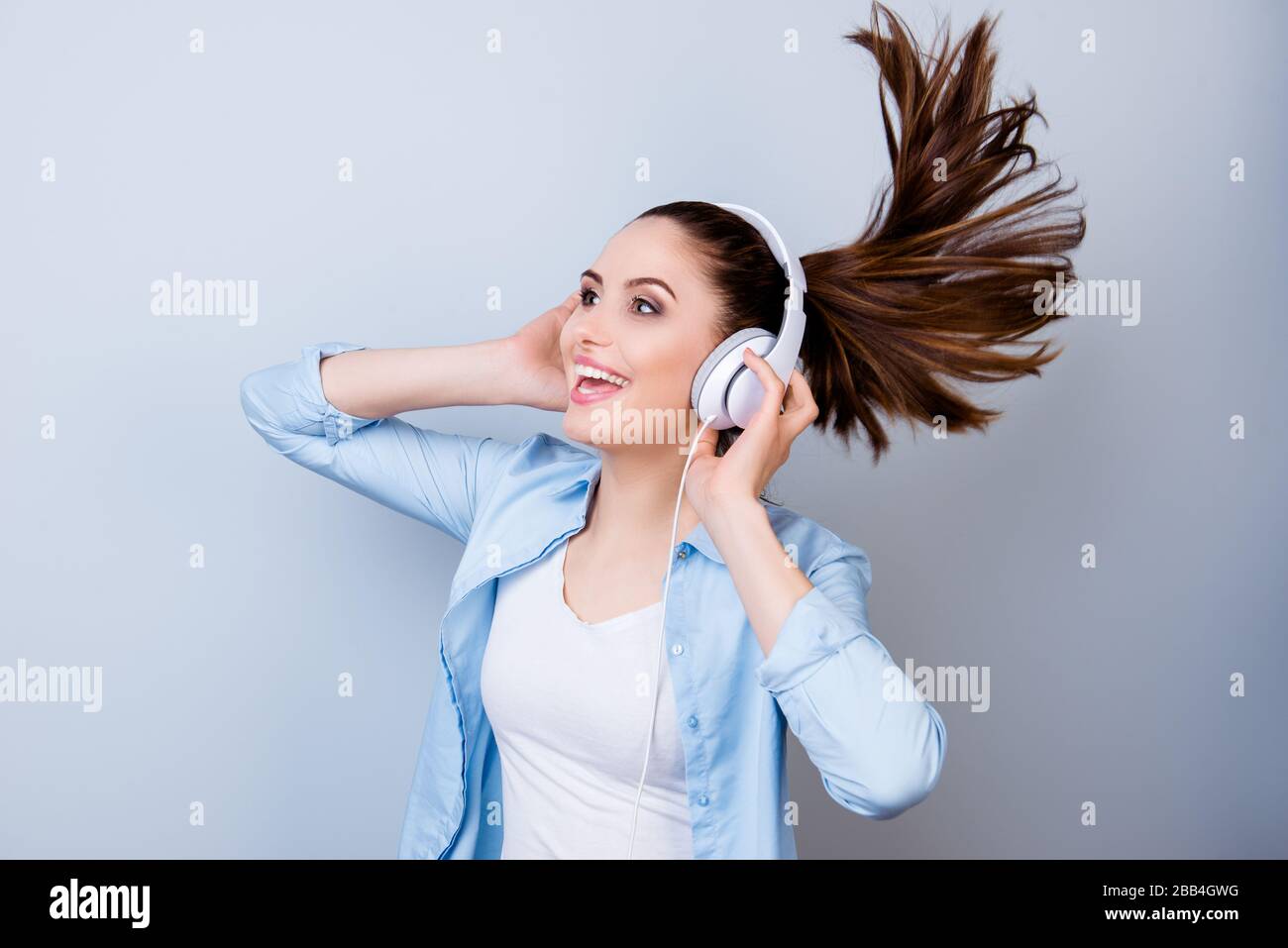 Cheerful smiling young woman in blue listening to music an headphones ...