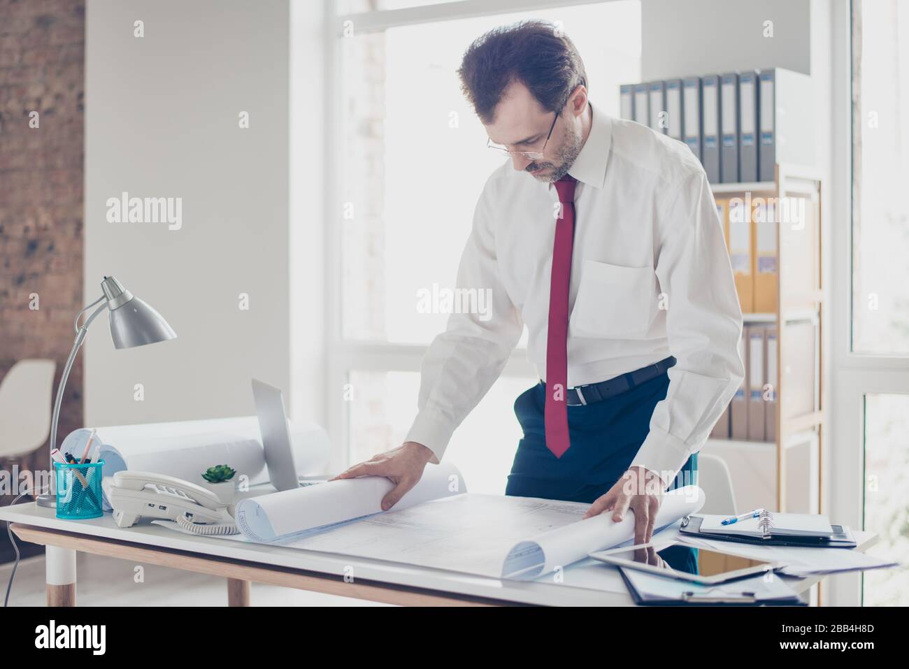 Close up photo of focused businessman working with scheme. He is standing by the table, studying the details of project Stock Photo
