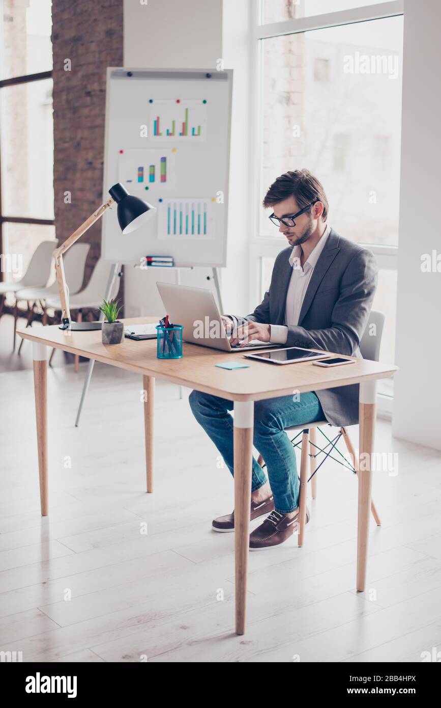 Full length of concentrated young businessman, which is browsing on his laptop at the office. He is handsome, successful, very stylish Stock Photo