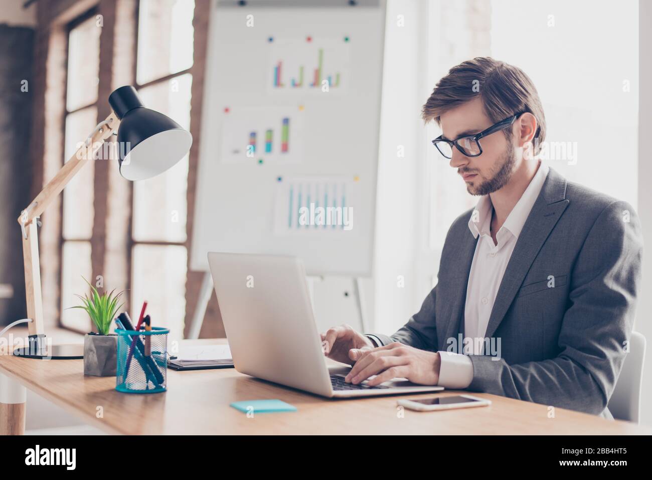 Concentrated young businessman is typing information on his laptop at the office. He is handsome, successful, very stylish Stock Photo