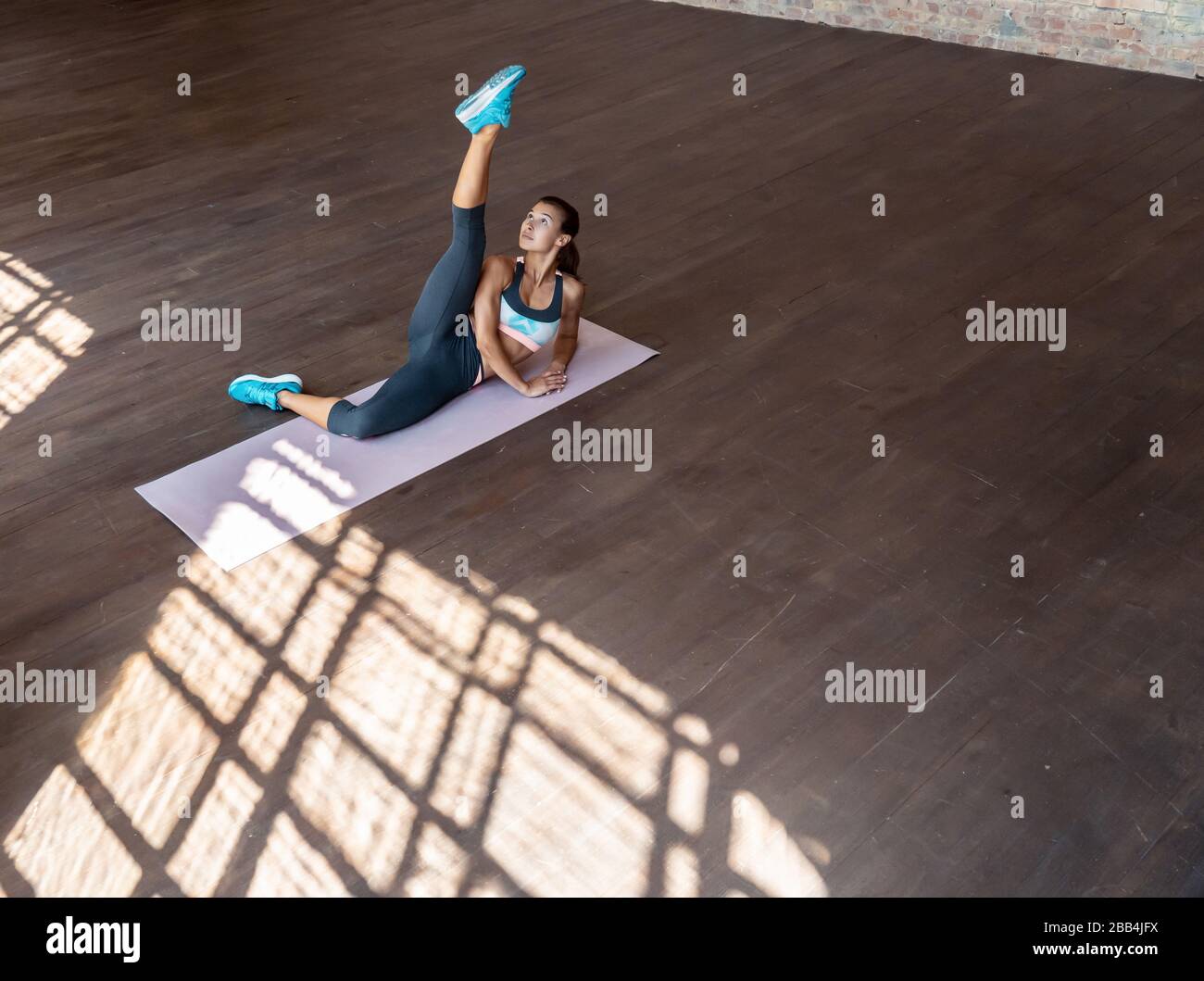 Fit active young woman stretch raising leg in gym, top view. Stock Photo