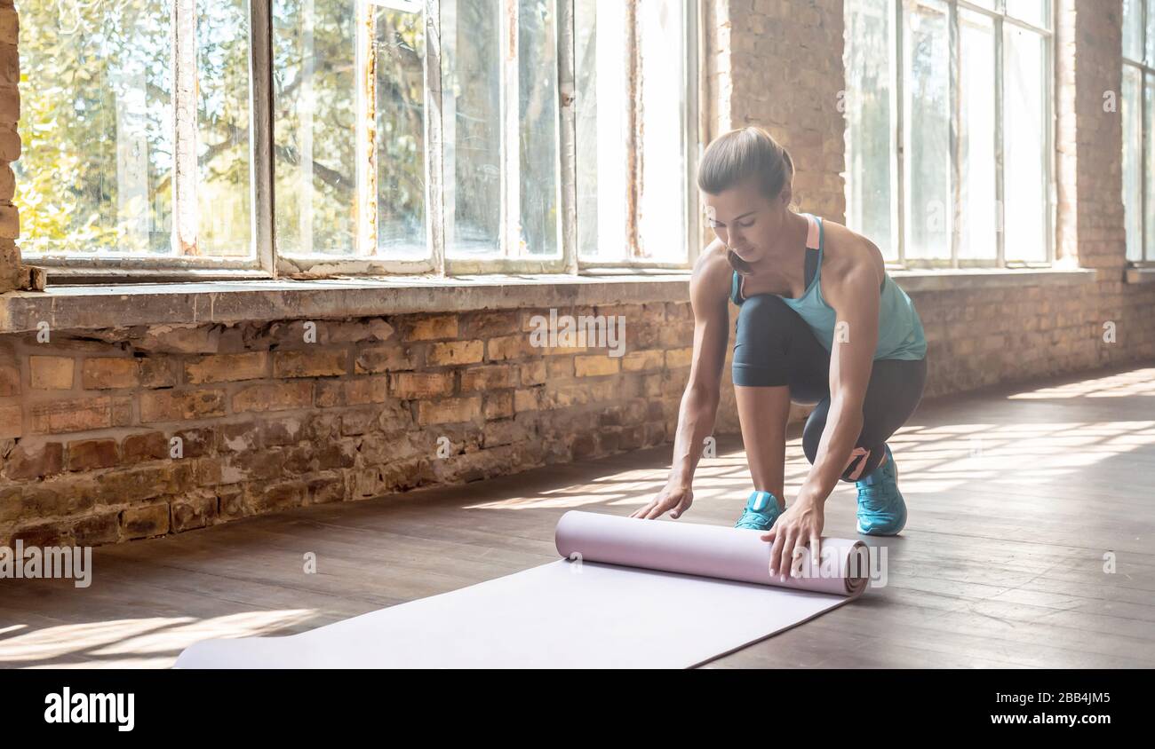Sporty fit young woman yoga instructor unrolling yoga mat in gym. Stock Photo