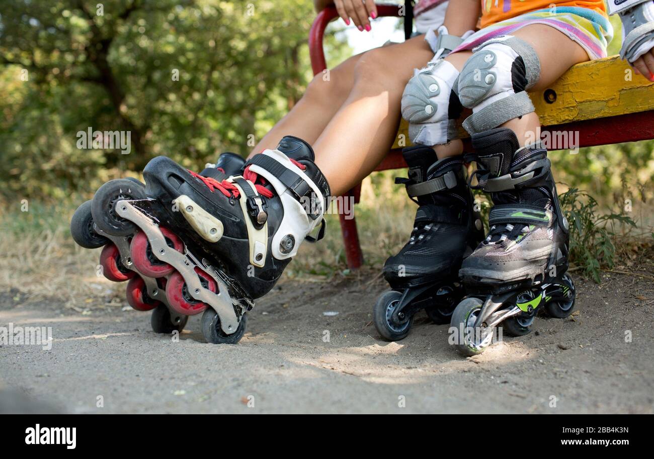 Cut view of children's legs with rollers in it. Kids sit on bench outside and have rest after skating. Two children with capknee and without Stock Photo