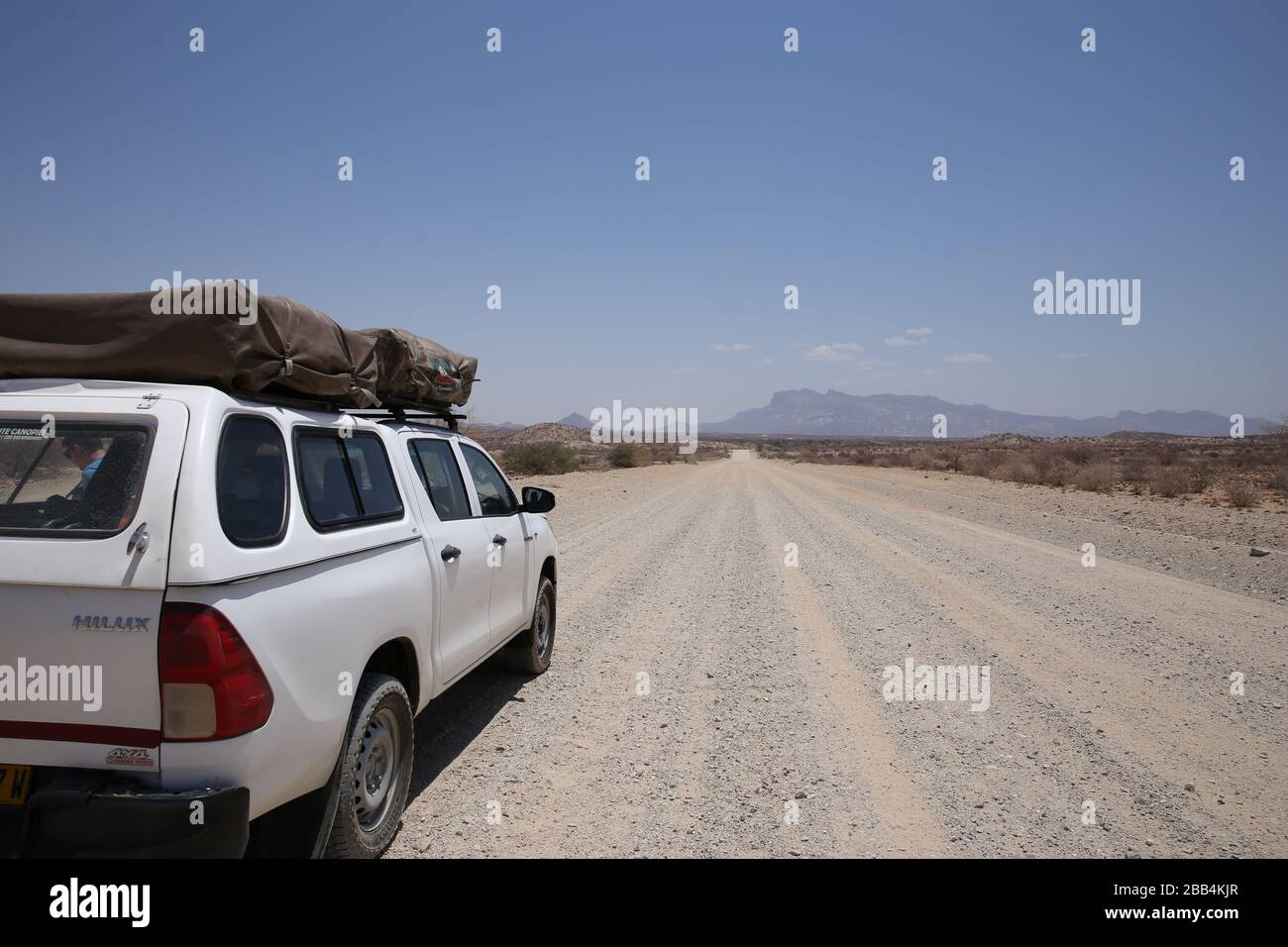 Long dirt road on the plains of Namibia stretch out in front of a 4x4 with roof top tents for camping Stock Photo