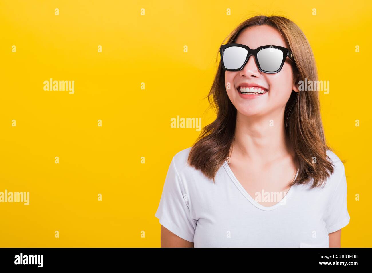 Portrait Asian Thai beautiful young woman happy smiling white teeth with sunglasses and looking side space, studio shot isolated on yellow background, Stock Photo
