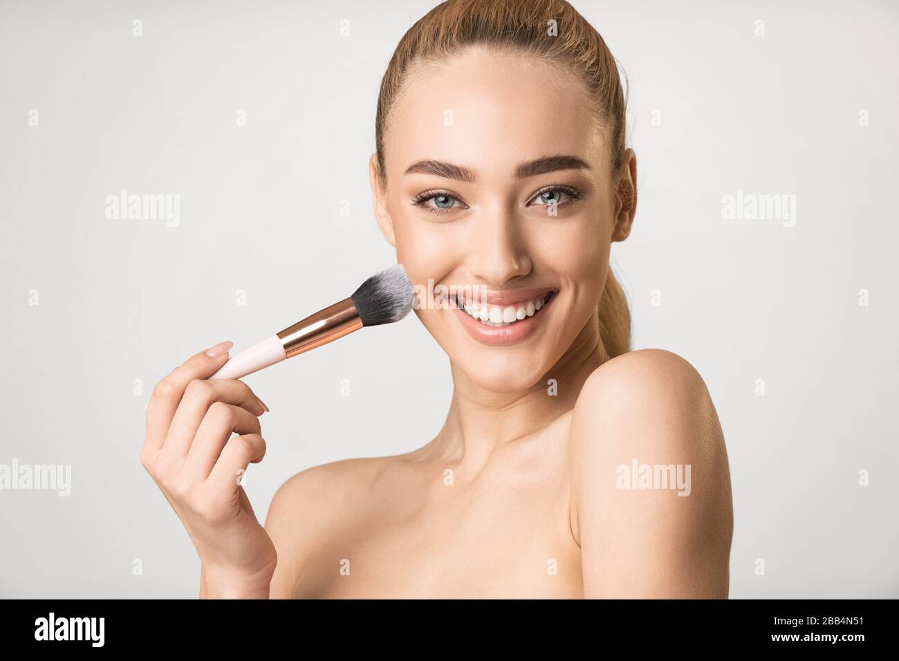 Woman Using Brush Applying Face Powder Posing On Gray Background Stock Photo