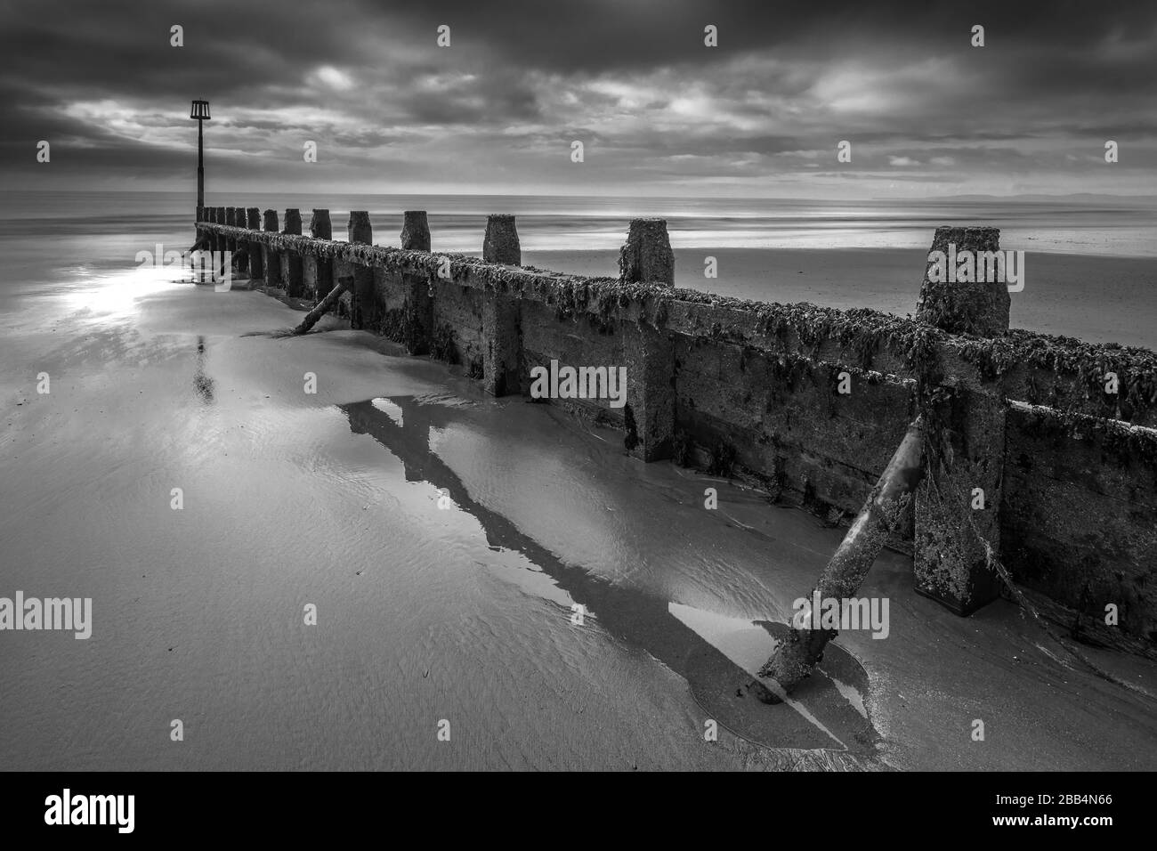 Sun rising over the ocean with water rushing around timbe groynes on ...