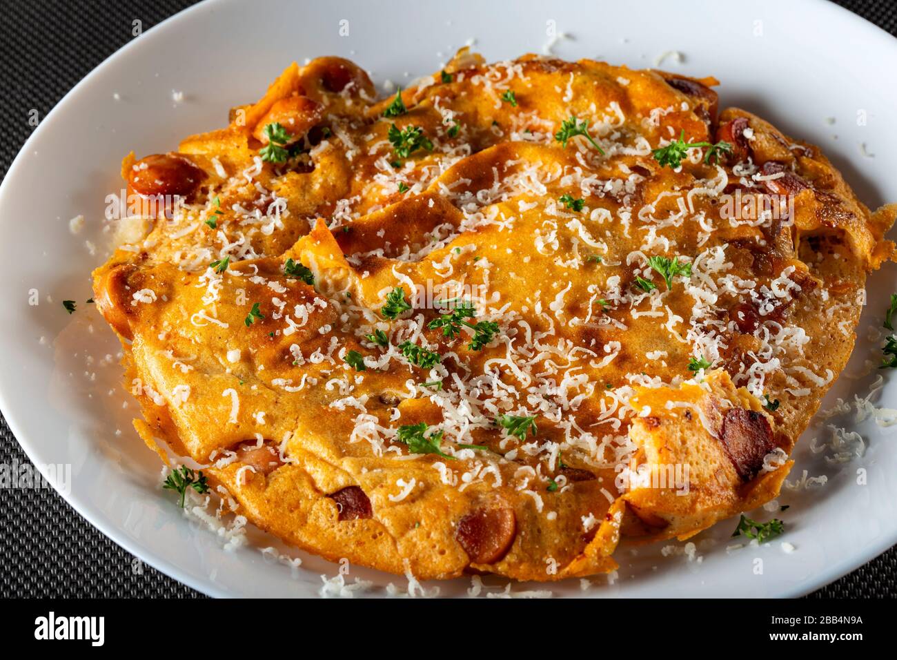 Fresh omelette with pork sausages, onion and gratted parmegiano on plate Stock Photo