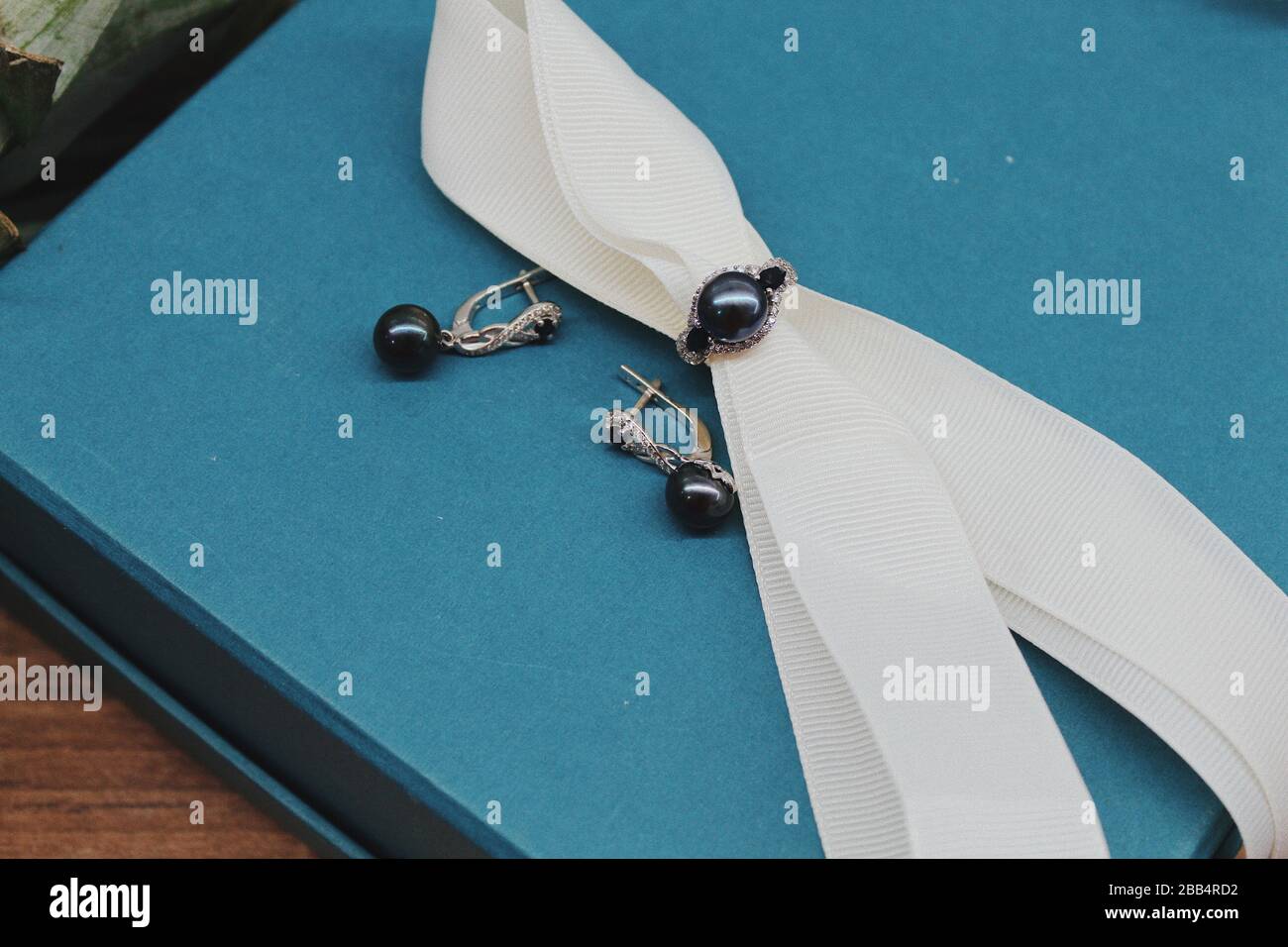 Closeup shot of a ring and earrings with black pearls on a blue jewelry box Stock Photo
