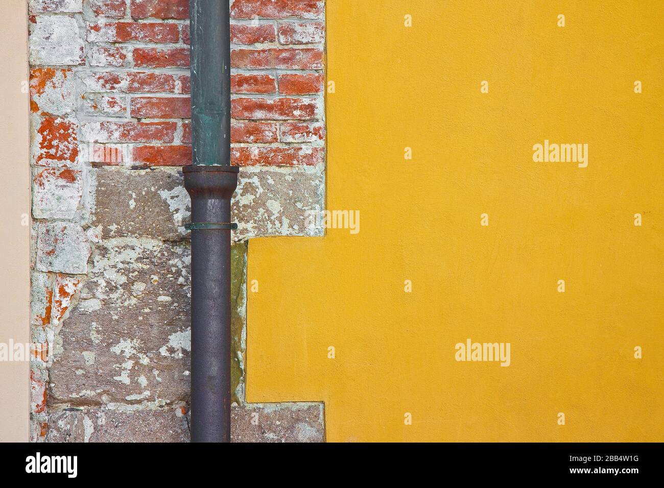 Old rusty copper and cast iron downpipe against a brick and plaster