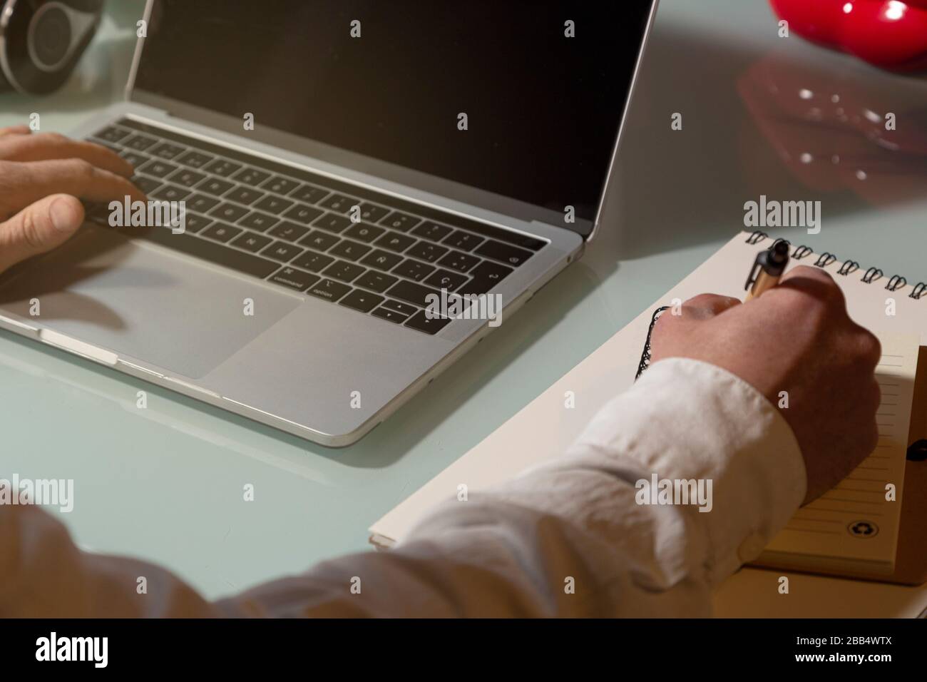 The hands of a businessman man who uses the laptop and takes notes working from home. Note pad and pen on the table. Telework concept Stock Photo