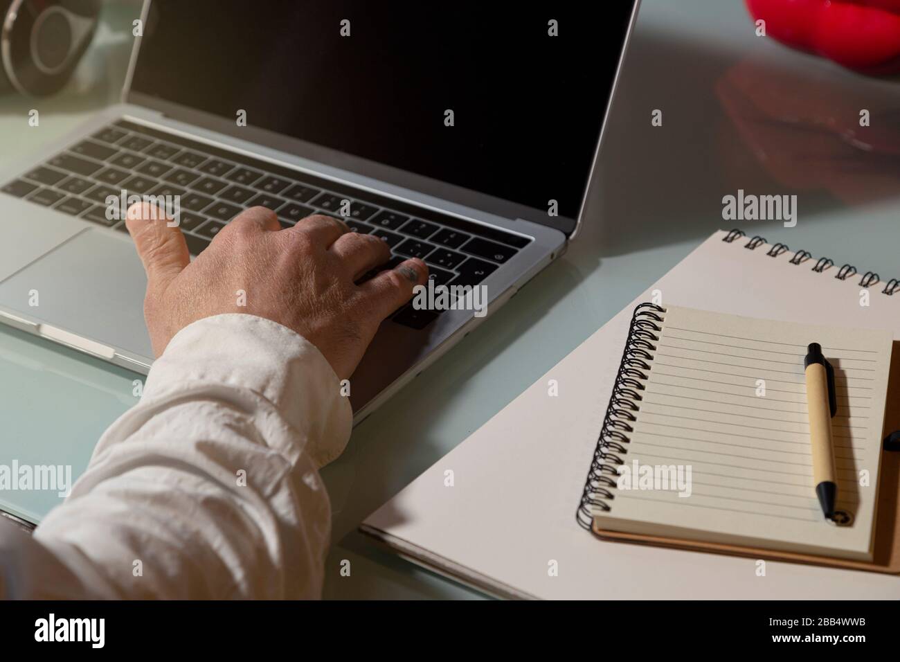 The hand of a man who uses the laptop to work from home. Note pad, pen on the table. Telework concept Stock Photo