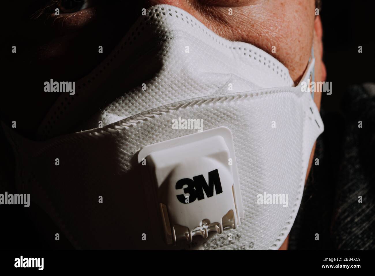 medical mask 3m n95 type on man looking away in light on black background coronavirus covid-19 Stock Photo